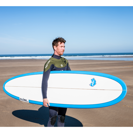 Person holding a surfboard on a beach with a clear blue sky