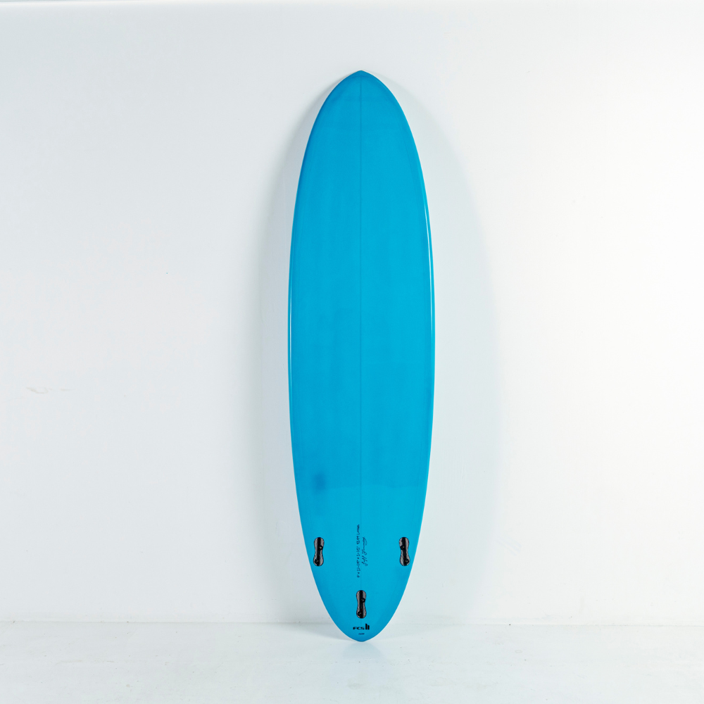 A bright turquoise blue egg surfboard standing vertically against a plain white wall, showing the bottom side with three black fins and small printed markings near the tail.