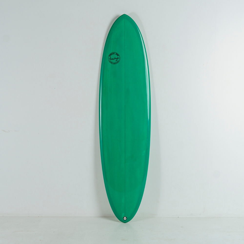 A glossy green egg surfboard standing vertically against a plain white wall, with a small circular logo near the upper center.