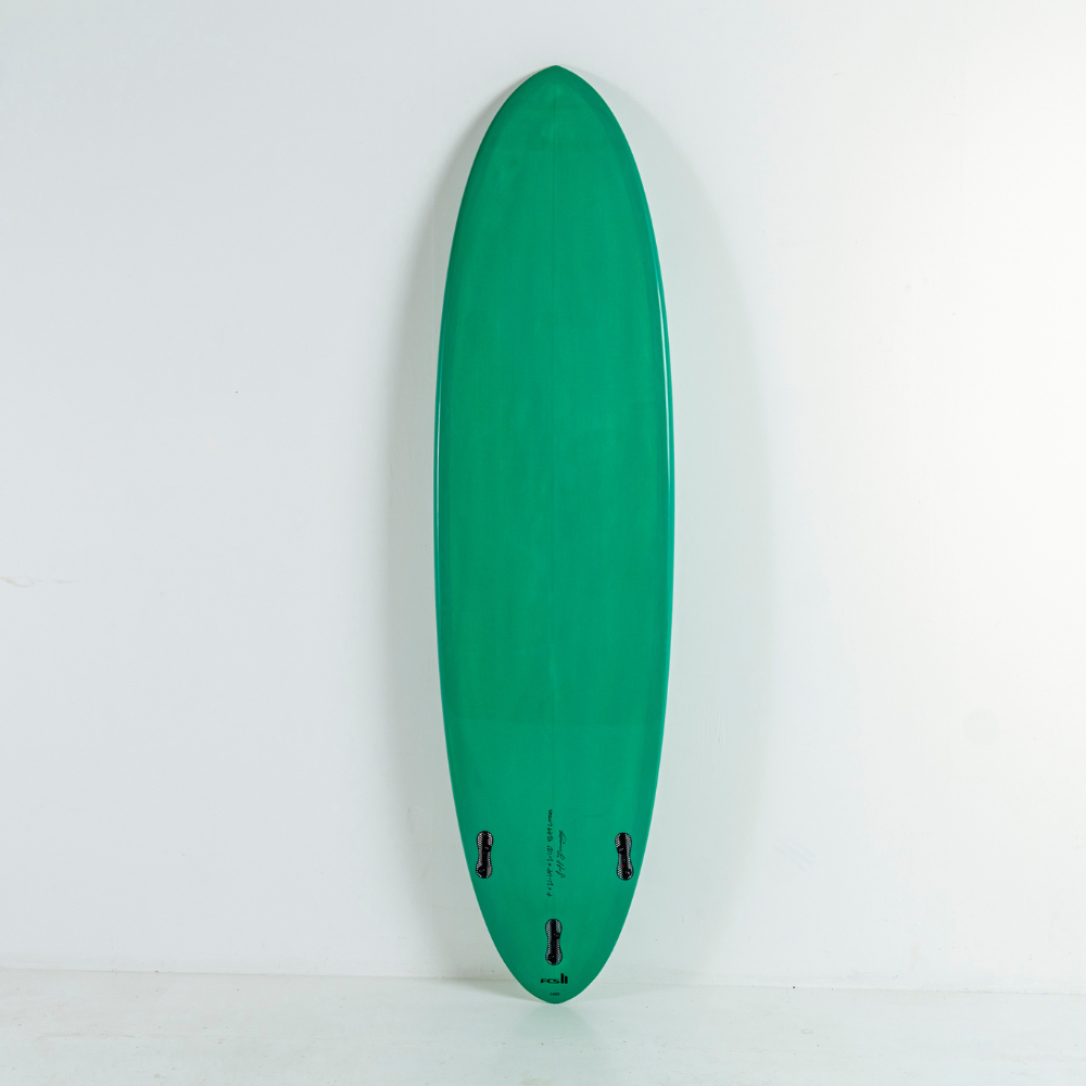 A green egg surfboard standing vertically against a plain white wall, with small black fin hardware visible near the tail.