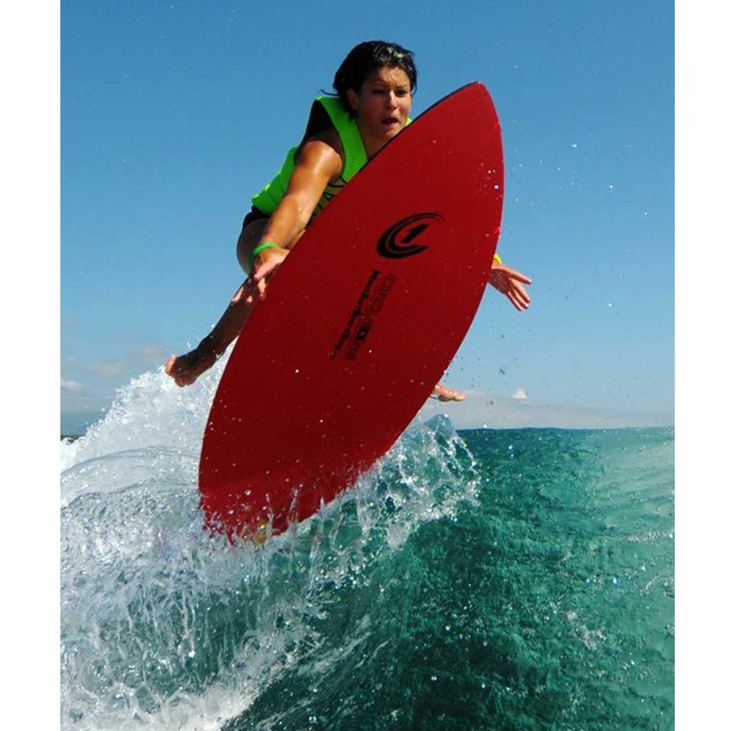 Person on a red skimboard in the air over a wave with a clear blue sky.