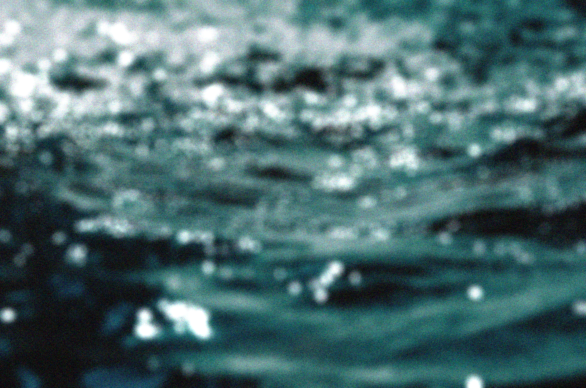 A close-up, abstract view of rippling water with teal-blue tones and bright white reflections.